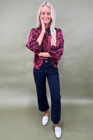 Woman wearing a red floral blouse and dark jeans against a plain background