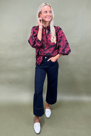 Woman wearing a red floral blouse and dark jeans against a green background