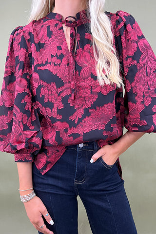 Person wearing a red and black floral blouse with blue jeans against a neutral background