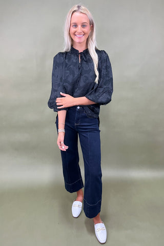 Woman wearing a dark denim outfit with white shoes on a plain background