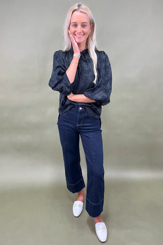 Woman wearing a dark denim shirt and jeans with white shoes on a plain background