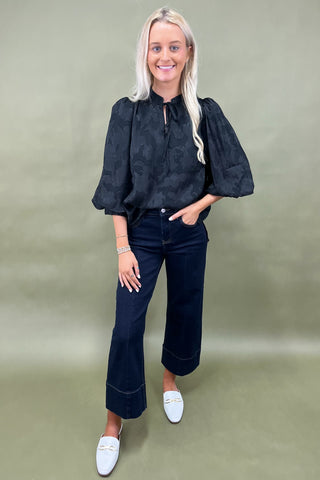 Woman wearing a black blouse and dark jeans against a green background