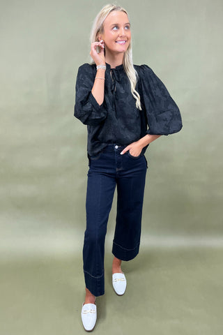 Woman wearing a black blouse and dark jeans on a green background