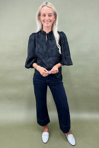 Woman wearing a black blouse and dark jeans against a green background