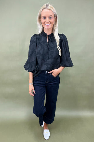 Woman wearing a black blouse and dark jeans against a green background