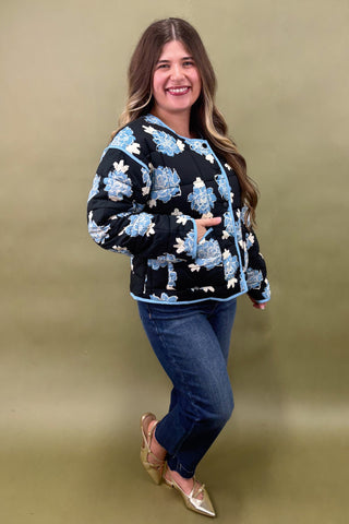 Woman wearing a black floral-patterned sweater and blue jeans against a beige background