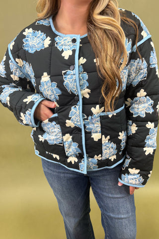 Person wearing a black floral-patterned jacket against a gold background