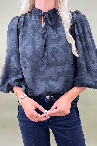 Person wearing a dark floral blouse with puffed sleeves against a neutral background