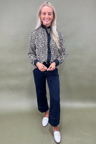 Woman wearing a patterned jacket, dark jeans, and white shoes against a plain background