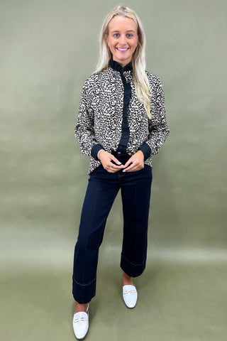 Woman wearing a patterned jacket, black top, and jeans on a green background