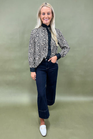 Woman wearing a patterned blouse, dark jeans, and white shoes on a green background