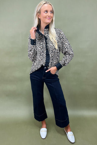 Woman wearing a leopard print jacket and dark jeans against a green background