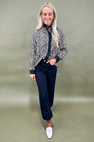 Woman wearing a patterned jacket and black pants on a plain background
