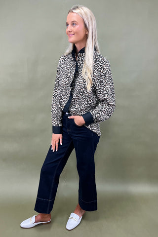 Woman wearing a patterned jacket and dark pants against a plain background