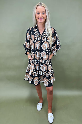 Woman wearing a patterned dress with white shoes against a green background