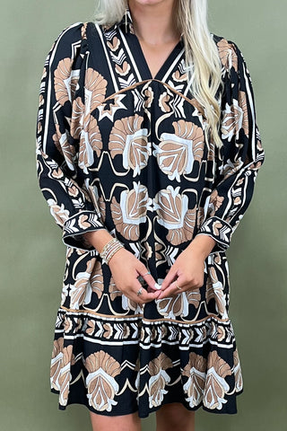 Person wearing a patterned dress with long sleeves against a green background