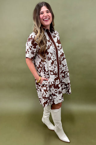 Woman wearing a floral dress with a brown zipper and white boots on a green background