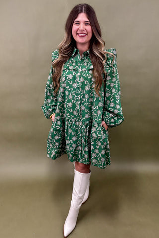 Woman wearing a green floral dress and white boots against a green background