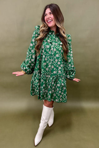 Woman wearing a green floral dress with white boots against an olive green background