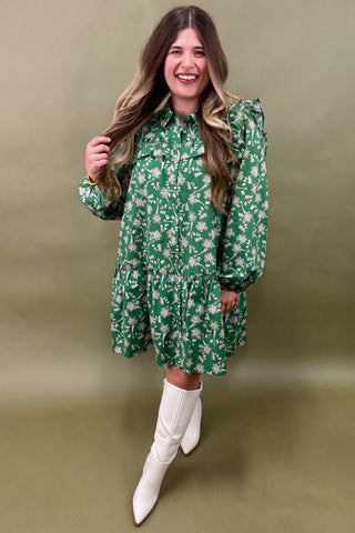 Woman wearing a green floral dress and white boots against an olive green background