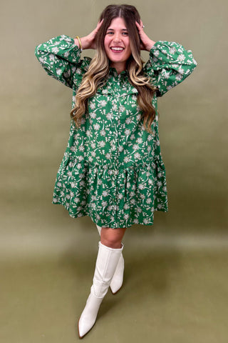 Woman wearing a green floral dress with white boots on a green background