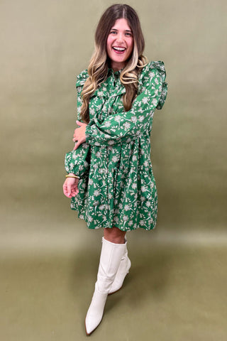 Woman wearing a green floral dress and white boots against a beige background