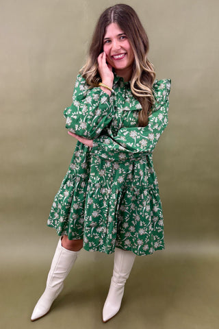 Woman wearing a green floral dress and white boots against an olive green background