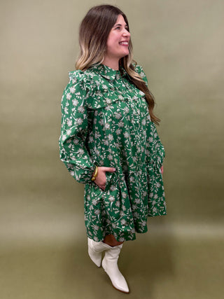Woman wearing a green floral dress and white boots against a beige background