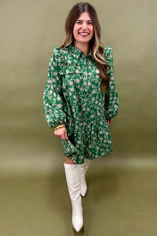 Woman wearing a green floral dress with white boots against an olive green background