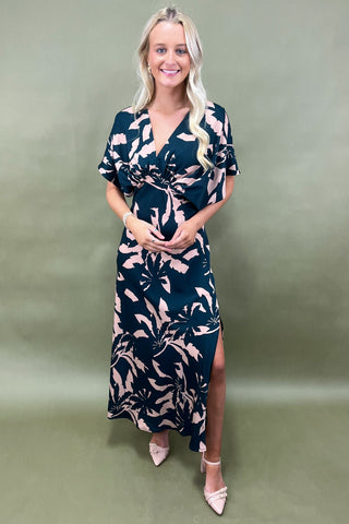 Woman wearing a navy dress with beige floral pattern on a green background