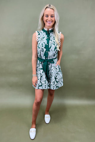 Woman wearing a green and white floral dress against a plain background