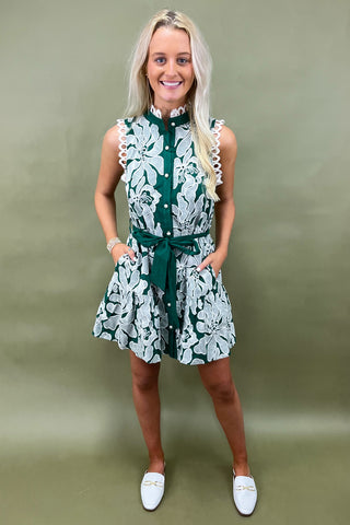 Woman wearing a green and white floral dress against a plain background