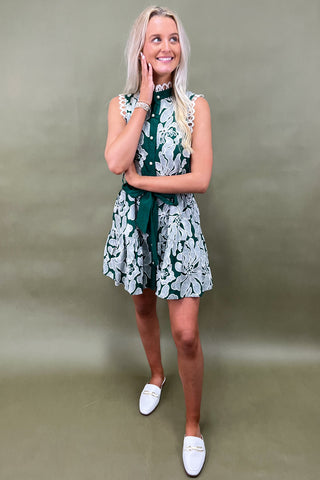 Woman wearing a green and white floral dress against a plain background