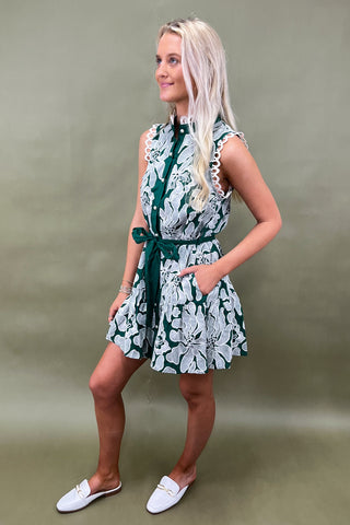 Woman wearing a floral dress with a green belt against a plain background