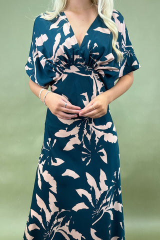 Woman wearing a blue dress with pink floral pattern against a green background