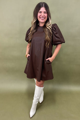 Woman wearing a brown dress with puffed sleeves and white boots on a green background