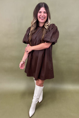 Woman wearing a brown dress and white boots against a green background