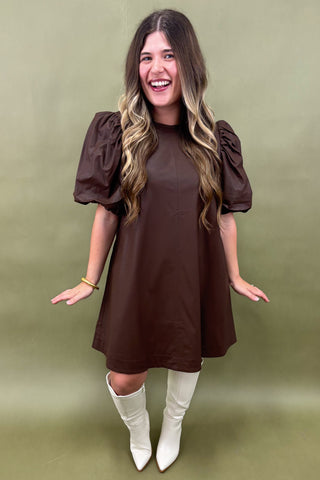 Woman wearing a brown dress with puffed sleeves against a green background