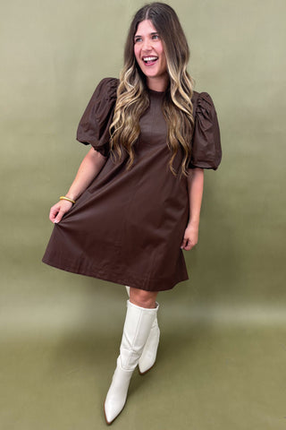 Woman wearing a brown dress with puffed sleeves and white knee-high boots on a green background