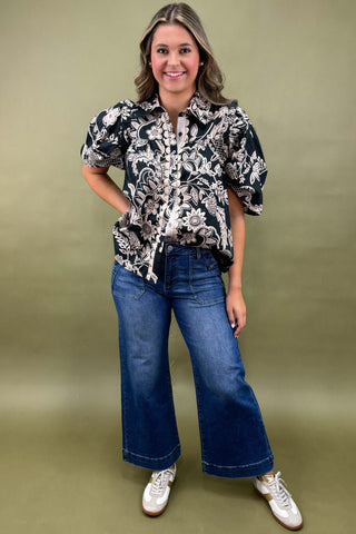 Woman wearing a black and white floral blouse with blue jeans on a green background