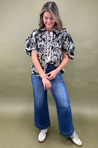 Woman wearing a black and white patterned blouse with blue jeans on a beige background