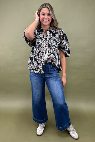 Woman wearing a patterned blouse and blue jeans against a green background
