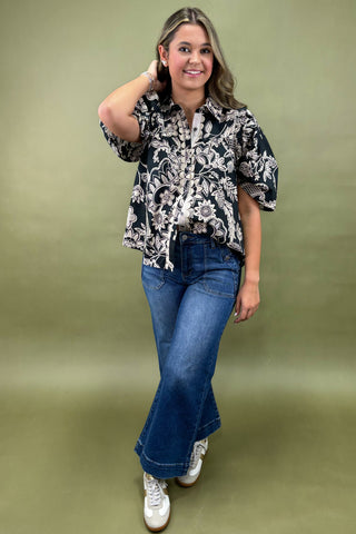 Woman wearing a black and white patterned blouse with blue jeans on a green background