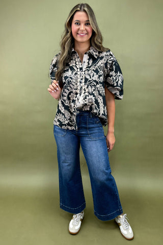 Woman wearing a patterned top and blue jeans against a green background
