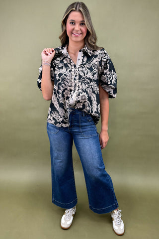 Woman wearing a black and white patterned blouse with blue jeans against a green background