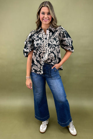 Woman wearing a black and white patterned blouse with blue jeans on a green background
