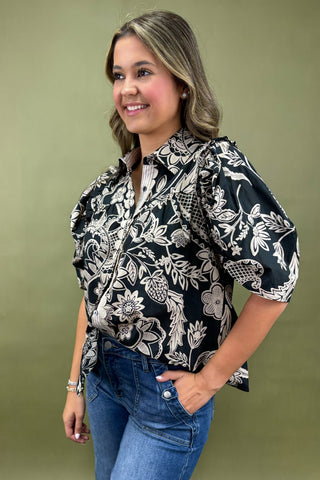 Woman wearing a black floral blouse with blue jeans against a green background