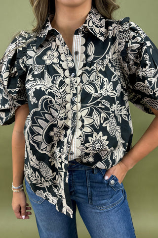 Person wearing a black and white floral patterned shirt with blue jeans on a green background
