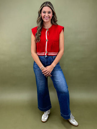 Woman wearing a red top with white buttons and blue jeans against a green background