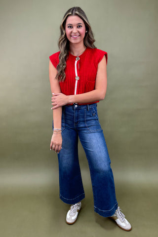 Woman wearing a red top and blue jeans against a green background